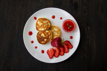 Three pancakes with cheese and strawberries and sauce on a white dish against wood background. Delicious cheese pancake and strawberries for the breakfast or lunch. Tasty meal with berries.