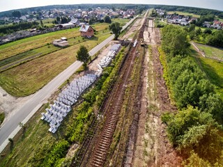Railway works in small village. Railroad construction and modernisation site. Aerial view on excavator and railway track components.  © Bartosz