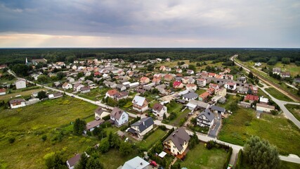 Fototapeta na wymiar Aerial view on small village located in central Poland. Summer landscape, cloudy afternoon. Green meadows, calm light. Small detached houses, streets, railroad.