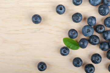  blueberry berries with green leaves on light wooden background top view 
