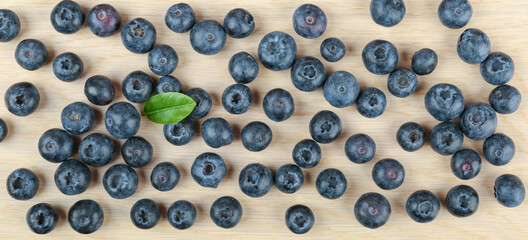  blueberry berries with green leaves on light wooden background top view 