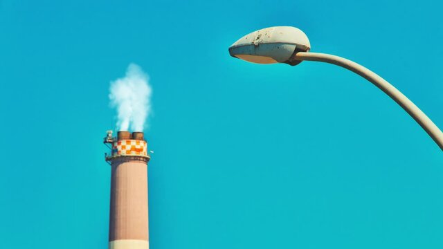 Cinemagraph of smoke emitted from the chimney of the Reading power plant and a modern street lamp. Tel Aviv, Israel. Concept of industry, pollution, electricity, or environmental protection. Loop.