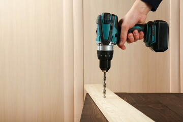 carpenter's hand is drilling wood plank by cordless drill close up with copy space