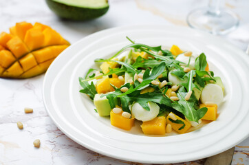 Avocado mango arugula pine nuts Mozzarella salad in a plate
