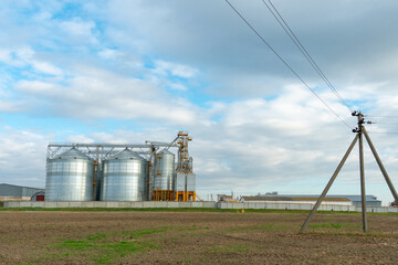 A large modern plant for the storage and processing of grain crops. view of the granary on a sunny day. Large iron barrels of grain. silver silos on agro manufacturing plant for processing and drying