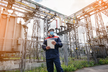 An electrical substation engineer inspects modern high-voltage equipment in a mask at the time of...