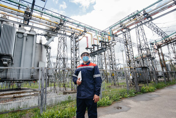 An electrical substation engineer inspects modern high-voltage equipment in a mask at the time of pondemia. Energy. Industry