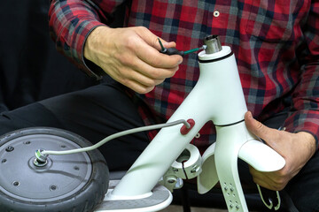 Electric scooter repair workshop. The master holds in his hand the broken part of the scooter and motor wheel. Replacing the tube and tires. Modern environmentally friendly mode of transport. © Pokoman