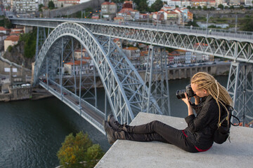 Young woman taking pictures in the downtown of Porto, Portugal. Dom Luis I Bridge over the Douro...