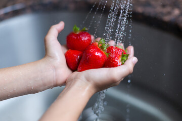 washing fresh strawberries under a sink faucet