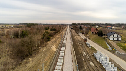 Fototapeta na wymiar Railway works in small village. Railroad construction and modernisation site. Aerial view on excavator and railway track components. 