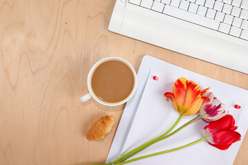 Work desk of a modern woman, home office. Cup of coffee latte, computer, notepad, tulips on a light table. Minimal business concept, healthy lifestyle, flat lay, place for text.