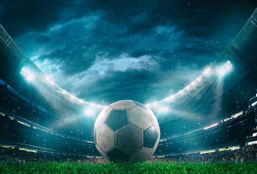 Close up of a soccer ball in the center of the stadium illuminated by the headlights