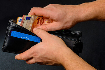 Man hand pulling money from wallet, black background and black wallet.