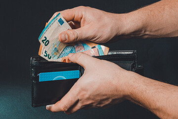 Closeup of human hands putting euro banknotes in wallet isolated on black background.