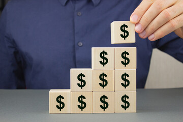 Closeup of a businessman making a pyramid of wooden cubes with a dollar sign on them. Financial...