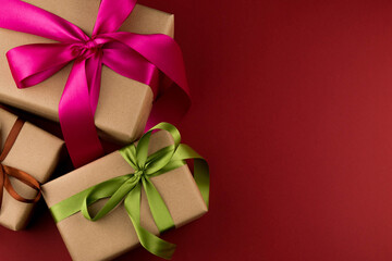 Three gift boxes in craft paper and tied with colored ribbons on a red background close-up with copy space