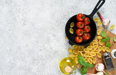 Raw pasta - Conchiglie with spices, tomatoes and basil on a concrete background. Top view.