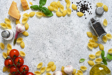 Food background with place for text. Raw pasta with spices, tomato and basil on a concrete background. Top view.