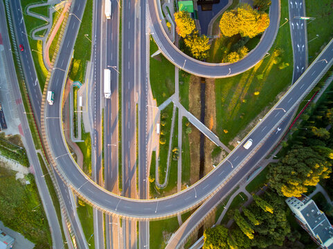 Top-down photo of large road traffic cord in sunlight. view on road junction in Warsaw in Poland. Several roads crossing on many levels. Grass and gren trees between overpasses and viaducts.