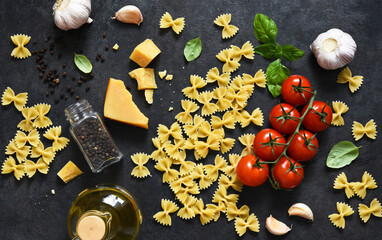 Raw farfolle with tomato and basil on a black background. Top view. Ingredients for making pasta