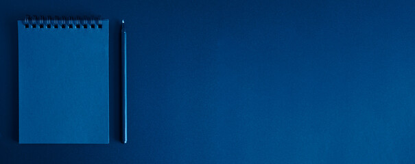 notebook on a spring and a pen on a black background. space for text. banner. toned classic blue...