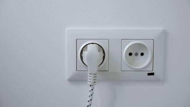 woman Inserts plug Into electrical socket on a white wall