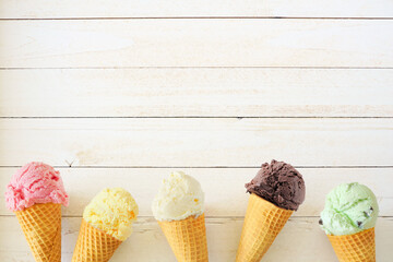 Ice cream cone bottom border with a variety of flavors. Top down view over a white wood background...