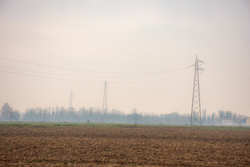 Campo sin cultivos con torres de electricidad y bosque de fondo en día de invierno 