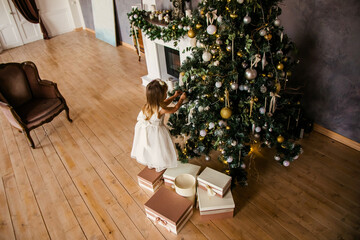 Cute little girl in the white dress with big presents near the Christmas tree