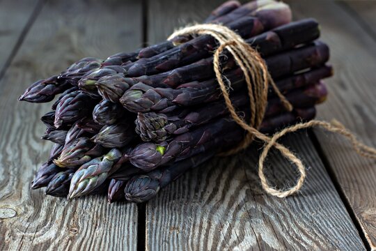 Fresh bunch of purple asparagus on a wooden background. - Powered by Adobe