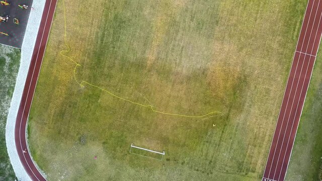 Top down aerial view of football field surface covered with green grass and sprinklers spraying water.
