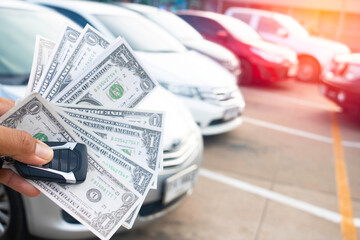 A hand holding a lot of dollars and car.A man holding dollars for cash on car.Money for sales...
