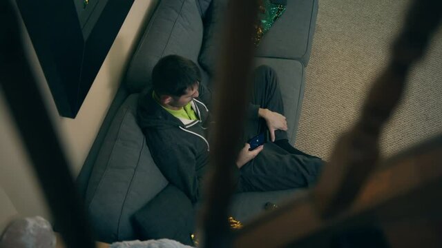 High quality close-up 4k slow motion video of a man sitting on a couch in his detached beautiful house main floor and watching television while browsing on the phone