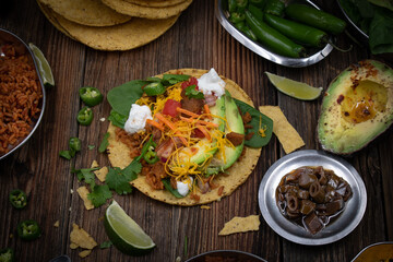 Vegetarian corn tostada with a variety of side toppings on wooden table