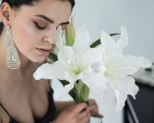 A very beautiful girl in her arms with beautiful white lilies sits on a chair on a white background
