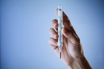 Thermometer in a woman's hand isolated on a clean background. Showing temperature. Fever measuring. Blue toning.