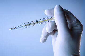 Doctor's hand in a latex glove holding thermometer. Temperature measuring. Blue toting.