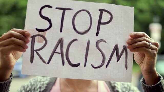 Young black Woman holds "Stop Racism" Poster in front of her Face