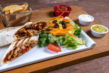 Burrito with grilled chicken and vegetables (fajitas, pita bread, shawarma). Mexican tortilla wrap with chicken breast and vegetables salad french fries and sauces. 
