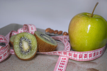 Red measuring tape, apple, kiwi and almonds on beige bathroom scales. Diet and Healthy life, loss weight, sport concept. Copy space. Isolated. White background