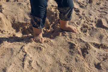 Baby toddler explores the life  on the sand beach. Feet of a toddler on the sand. Concept of exploration, travel, and summer