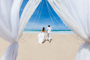 Newlyweds holding hands hugging at white sandy tropical caribbean beach landscape after wedding...