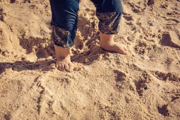 Baby toddler explores the life  on the sand beach. Feet of a toddler on the sand. Concept of exploration, travel, and summer