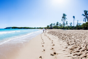 Newlyweds holding hands hugging at white sandy tropical caribbean beach landscape after wedding ceremony of marriage on destination wedding honeymoon travel looking on blue sea in Punta Cana Dominican