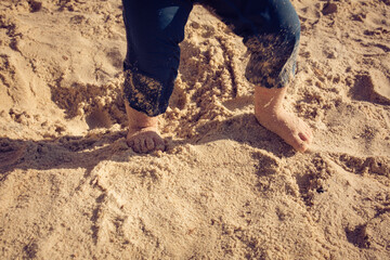 Baby toddler explores the life  on the sand beach. Feet of a toddler on the sand. Concept of exploration, travel, and summer