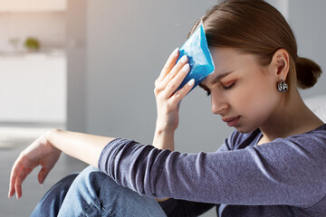 Woman applying ice pack as cold compress on forehead due to headache, migraine, tired after work,...