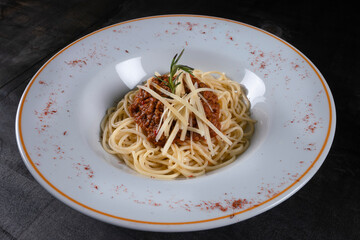 Pasta spaghetti with minced meat, cheese and rosemary in a bowl on a black wooden background. Side view with copy space.
