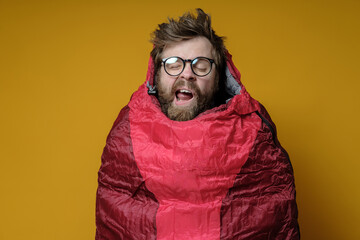 Funny, yawning man in a sleeping bag on a yellow background, he sleeps and imaginary himself in a wonderful travel.