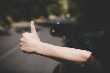 Young happy man drives a car and holds his hand out from the window. Driver enjoys driving and shows Ok sign with his hand out of window. Road trip, travel and freedom concept.
